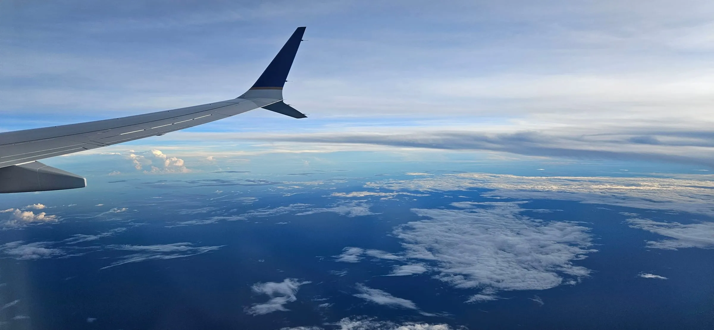 An aeroplane wing over a sea of clouds, with the ocean far below